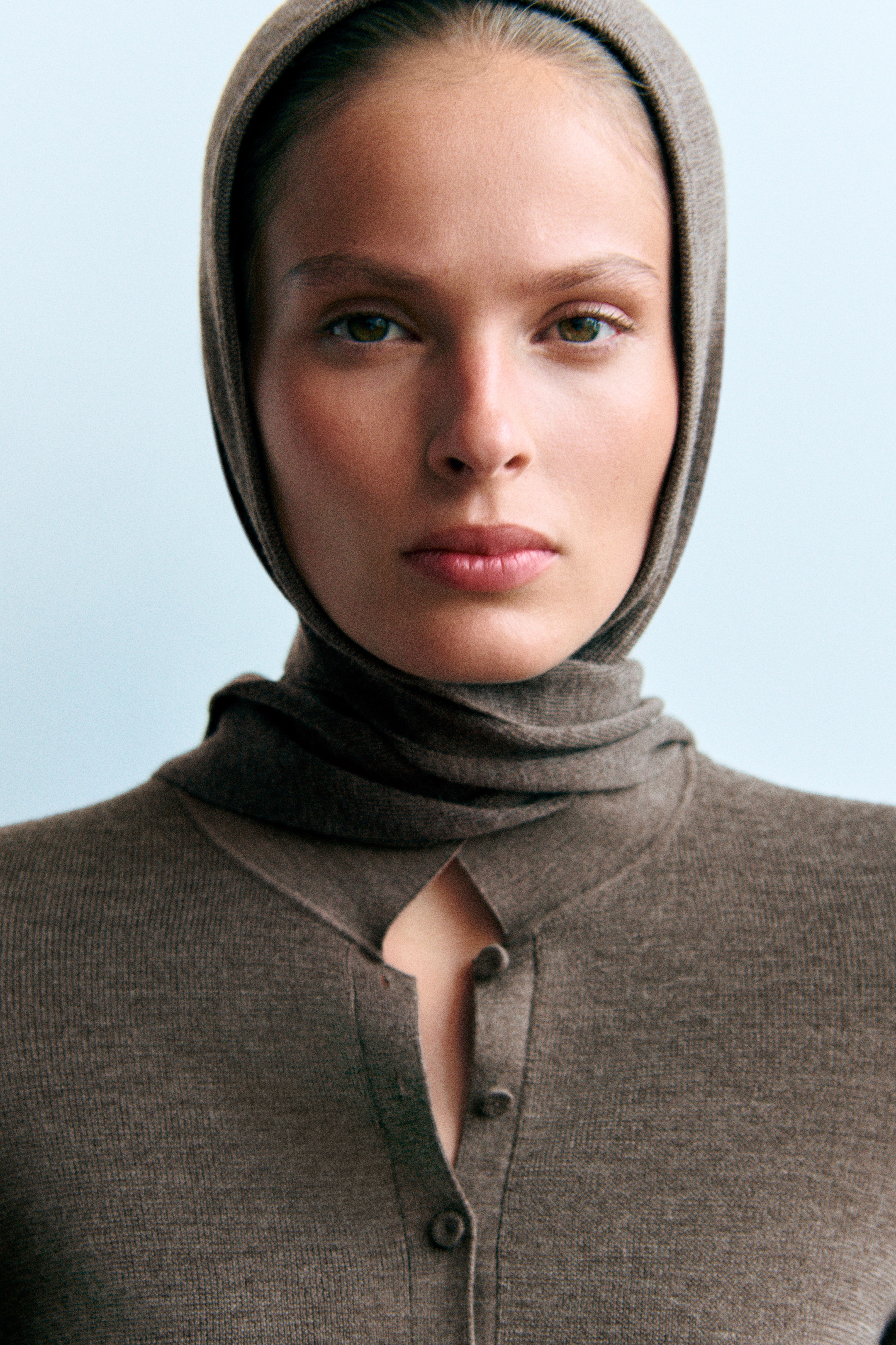 A person wearing a brown buttoned top with a matching hood.