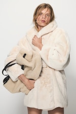 Placeholder for: Person wearing a fluffy cream coat, holding a matching bag against a plain background.