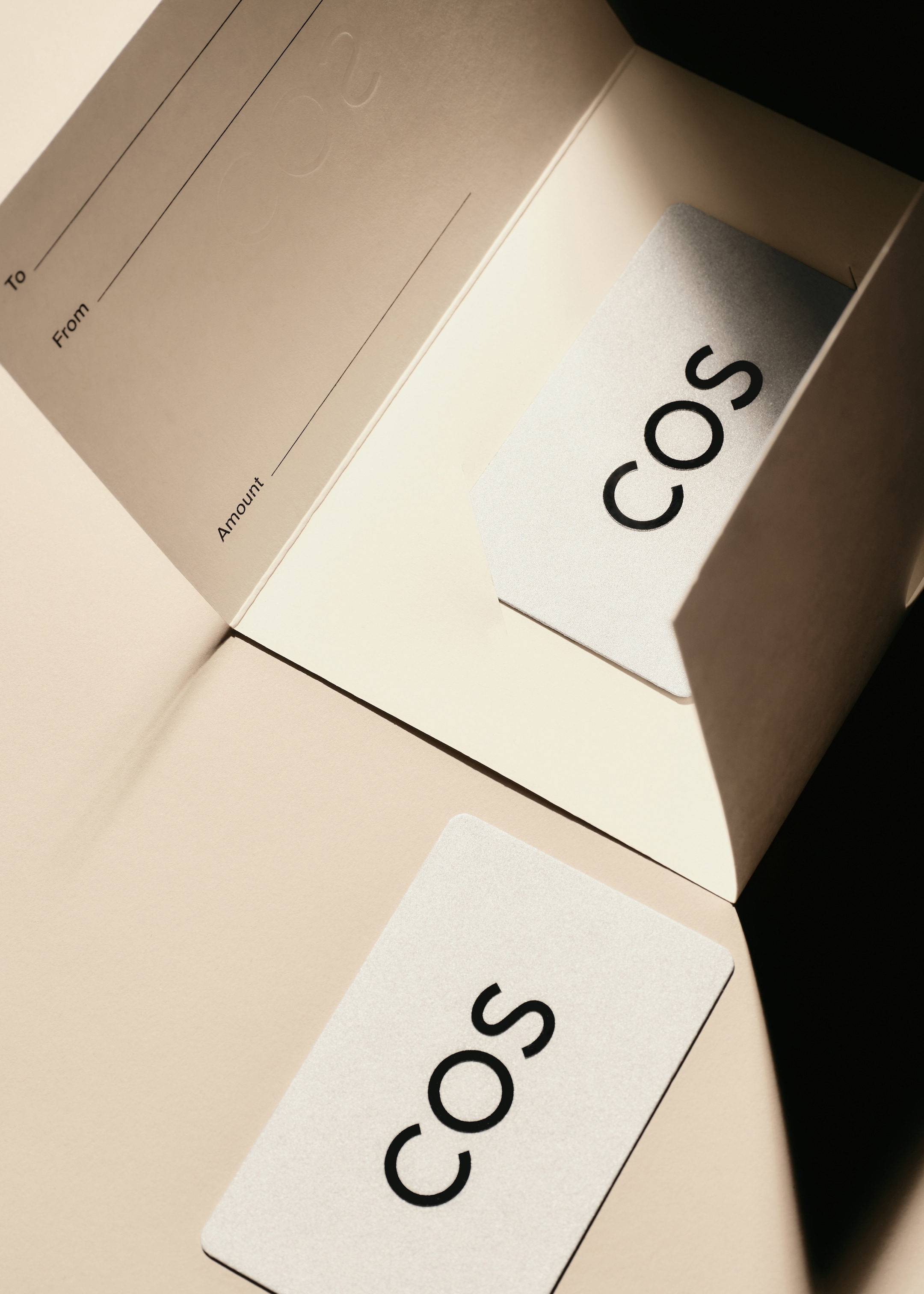 A COS gift card partially inserted into an envelope, with sections for "To," "From," and "Amount" visible on the envelope.