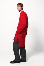 Placeholder for: Person wearing a red oversized sweater, gray pants, and black shoes, standing against a plain white background.