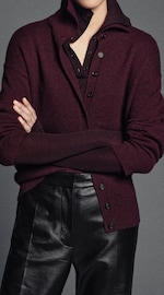 Placeholder for: Woman in a burgundy button-up sweater and leather pants with arms crossed, shown from neck to waist against a neutral background.