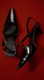 Placeholder for: Black strappy high-heeled shoes with a crocodile pattern, set against a rich red background.