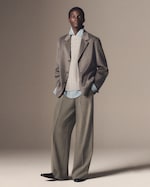Placeholder for: A person in a gray blazer, cable-knit sweater, and light blue shirt, with wide-legged trousers, standing against a neutral background.