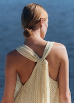 Placeholder for: Back view of a person with blonde hair tied in a bun, wearing a light, dotted dress against a blurred blue background.