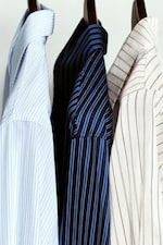 Placeholder for: Three striped shirts on hangers: light blue, dark blue, and white shirts with varying stripe patterns.