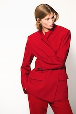 Placeholder for: Person in a bold red suit with an asymmetrical jacket, posing against a plain white background.