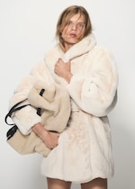 Placeholder for: Woman in a white faux fur coat holding a matching bag, standing against a plain background.