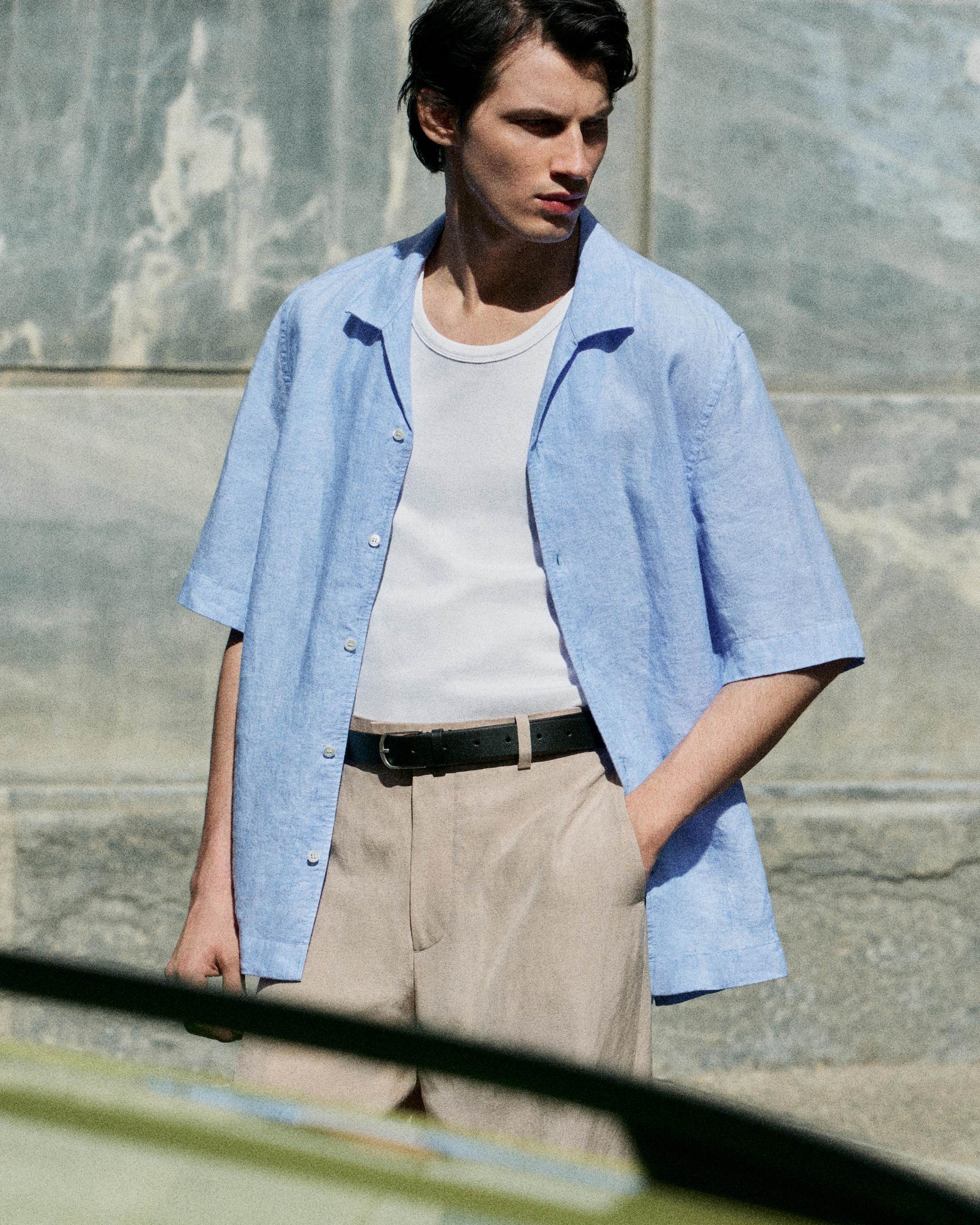 model wearing blue linen shirt on top of white vest and beige linen trousers
