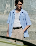 Placeholder for: model wearing blue linen shirt on top of white vest and beige linen trousers
