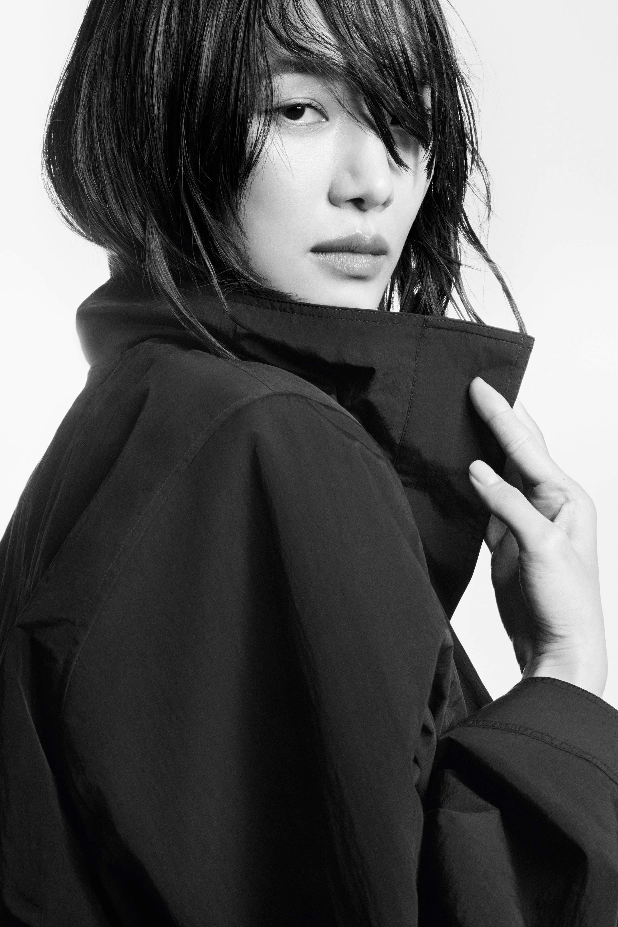 Black and white photo of a person with wet hair, wearing a dark jacket and looking over their shoulder with a serious expression.