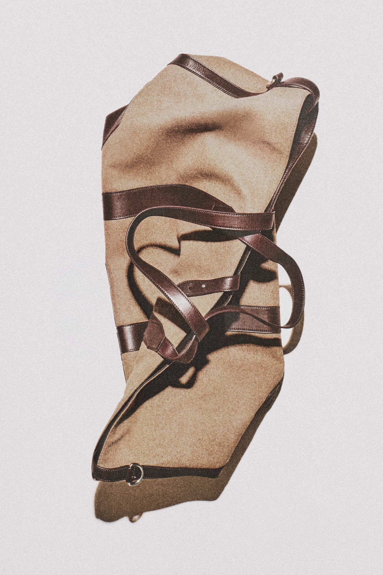 Tan canvas duffel bag with dark brown leather straps and trim, laid flat on white background casting a soft shadow.