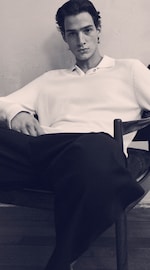 Placeholder for: Black & white image of a man in a knitted white polo shirt & black trousers on, sitting down