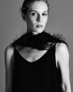 Placeholder for: Black and white portrait of a woman wearing a sleeveless black dress and a feathered accessory around her neck, looking towards the camera.
