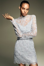 Placeholder for: Person wearing a light blue lace dress in a poised pose against a neutral background.