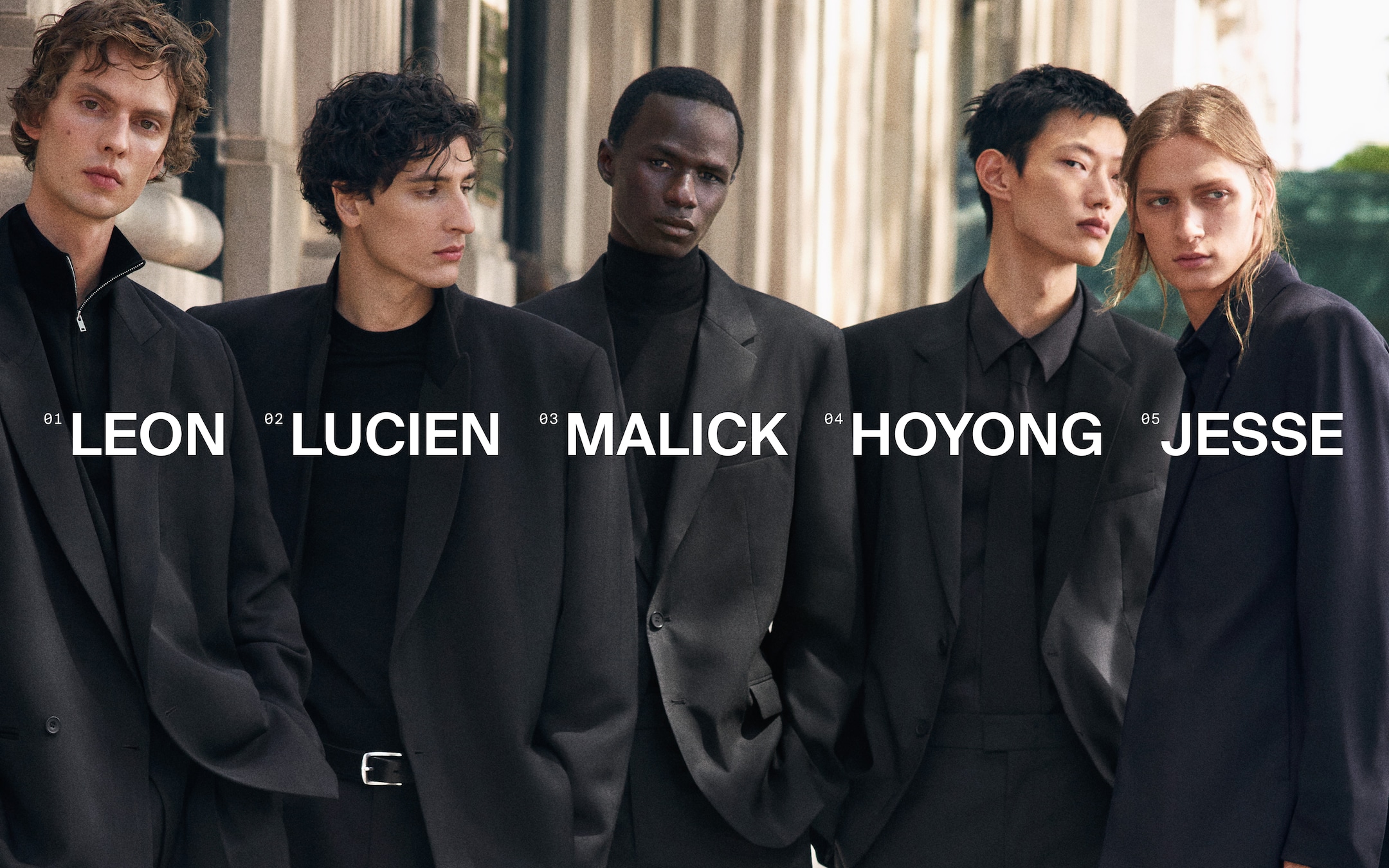 Five individuals in stylish black suits stand close together outdoors, with names displayed prominently over each person.
