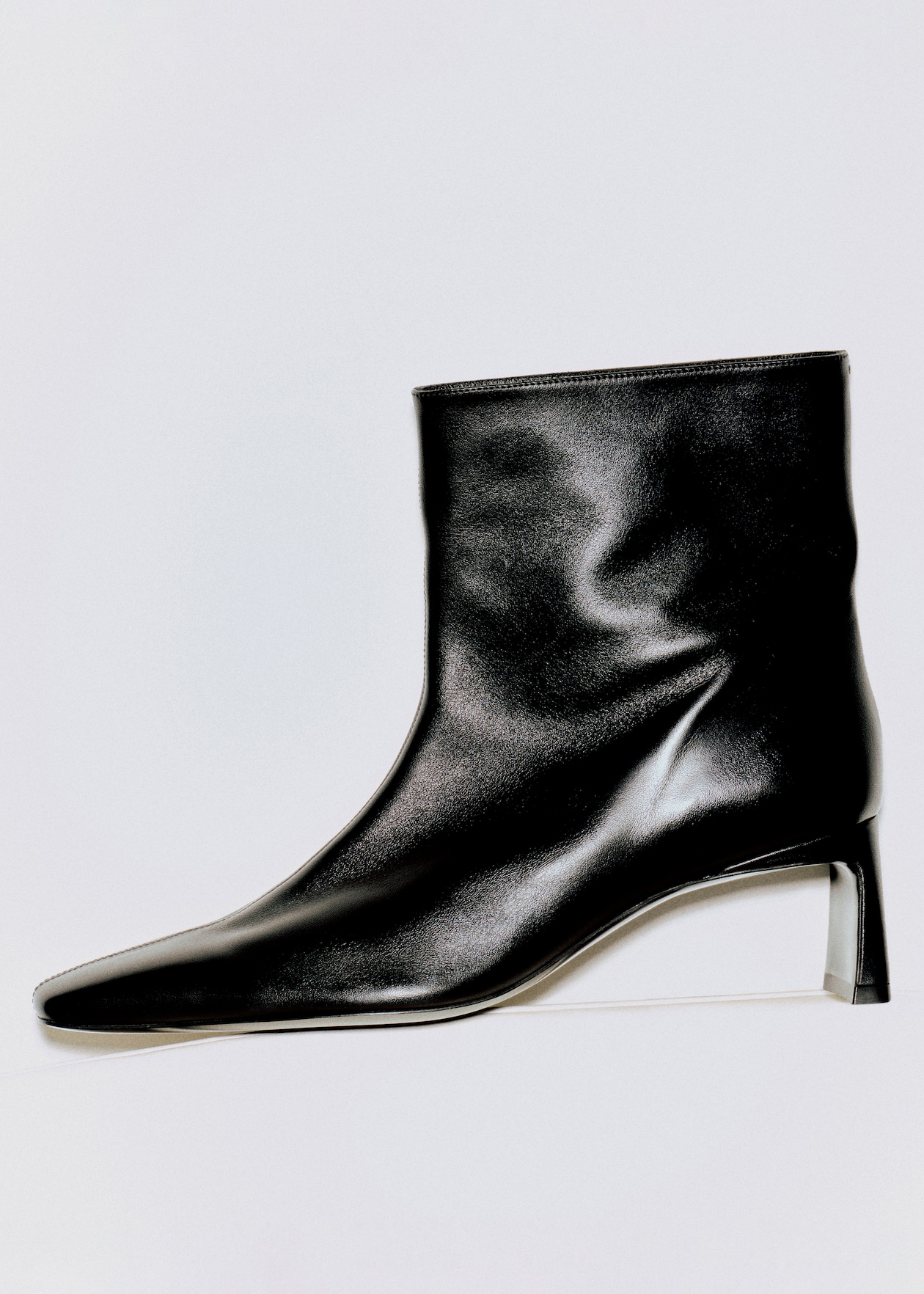 A sleek black leather ankle boot with a pointed toe and a low heel, displayed against a white background.