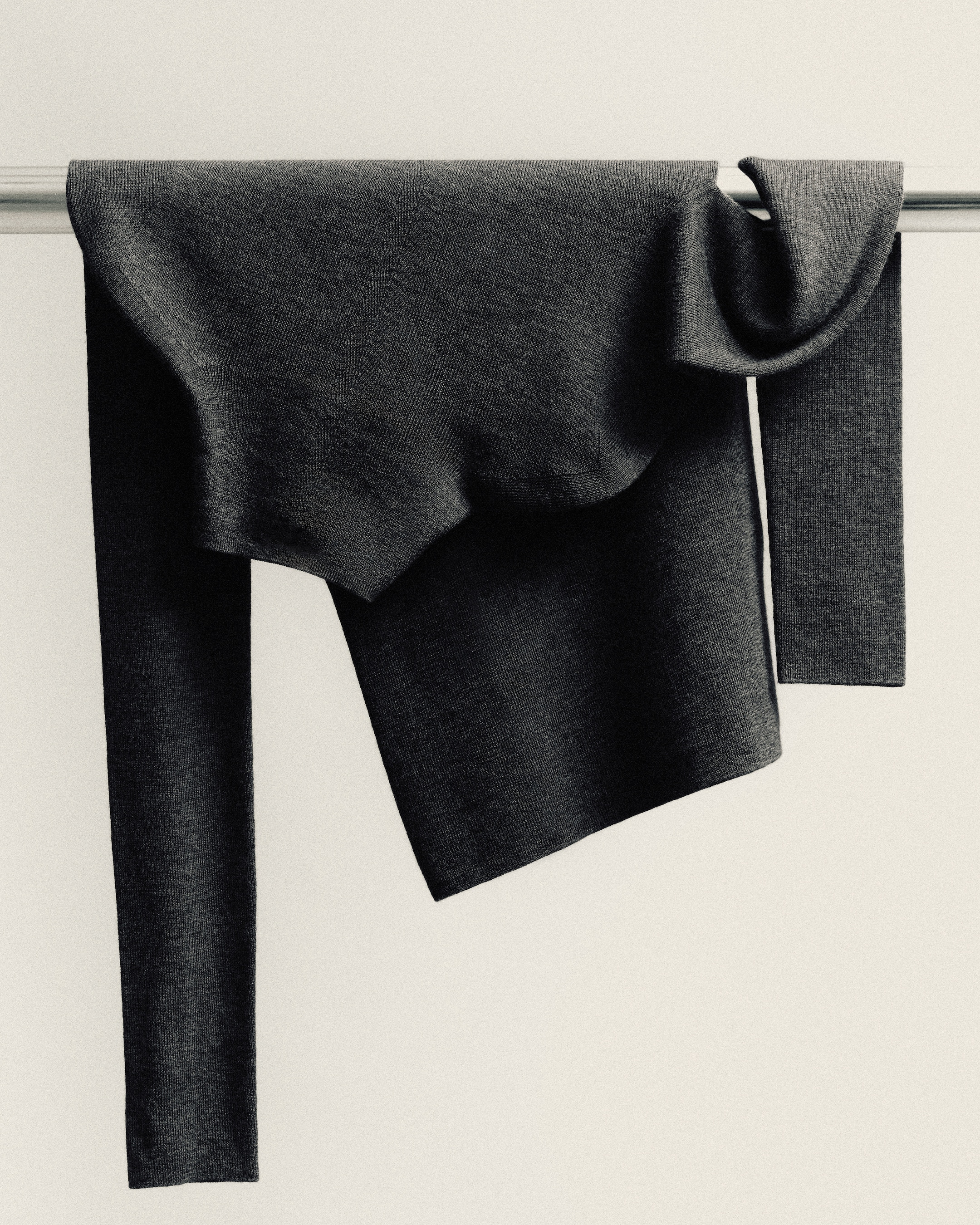A dark gray sweater casually draped over a metal rod, creating soft folds and shadows against a plain light background.