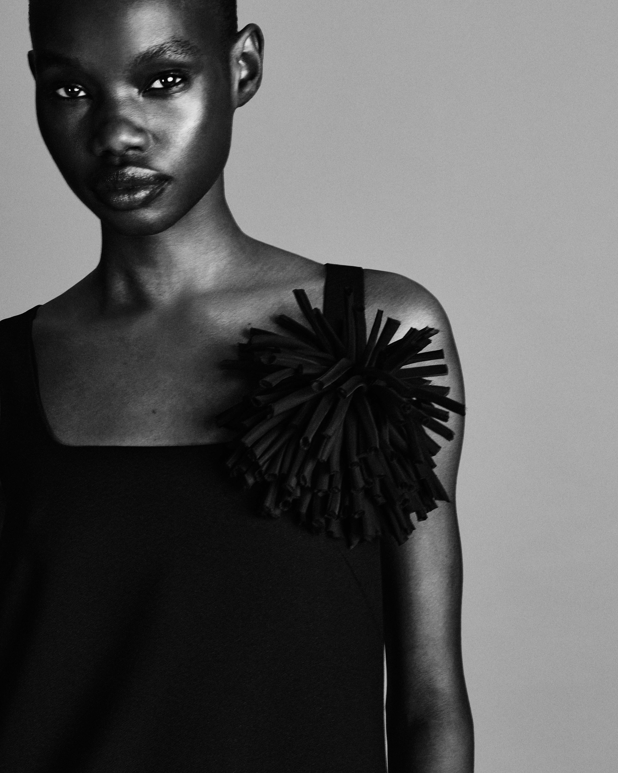 Black and white portrait of a person with short hair wearing a sleeveless top adorned with an abstract embellishment on the shoulder.