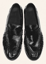 Placeholder for: A pair of shiny black leather slip-on loafers with pleated detailing on the uppers, viewed from above on a light background.