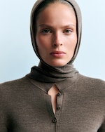 Placeholder for: Person gazing forward, wearing a brown headscarf and sweater with a light blue background.