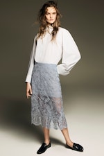Placeholder for: A model wearing a white striped blouse, a light blue lace skirt, and black loafers poses against a neutral background.