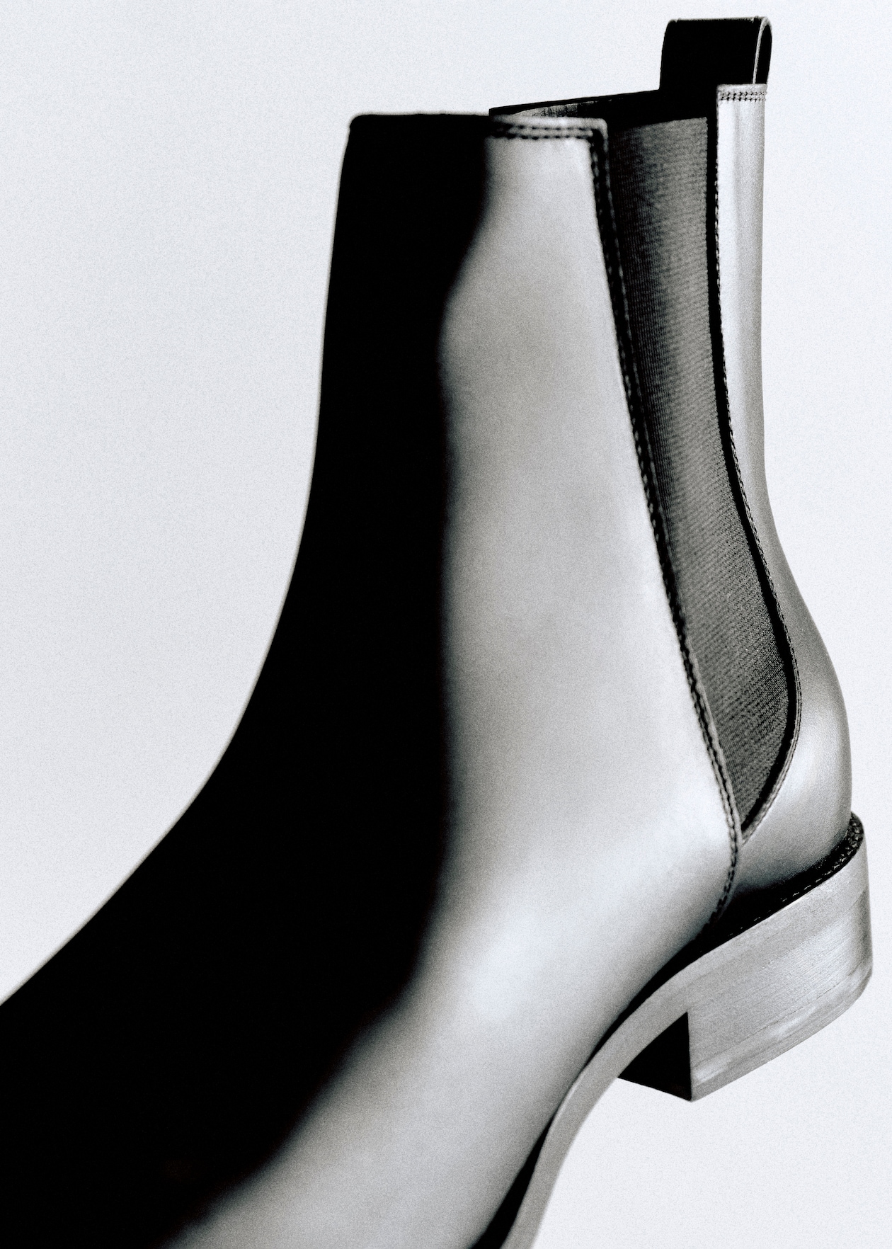 Close-up of a sleek black leather Chelsea boot with elastic side panel, set against a plain background.