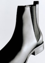 Placeholder for: Close-up of a sleek black leather Chelsea boot with elastic side panel, set against a plain background.