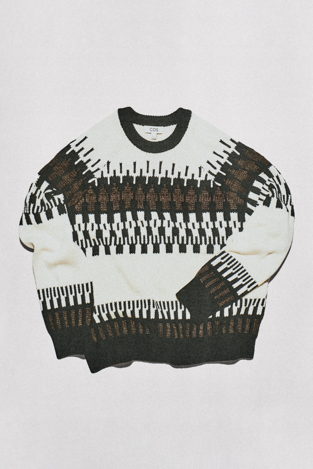 Cream and black patterned knit sweater (COS) with geometric Fair Isle design, laid flat on white background.