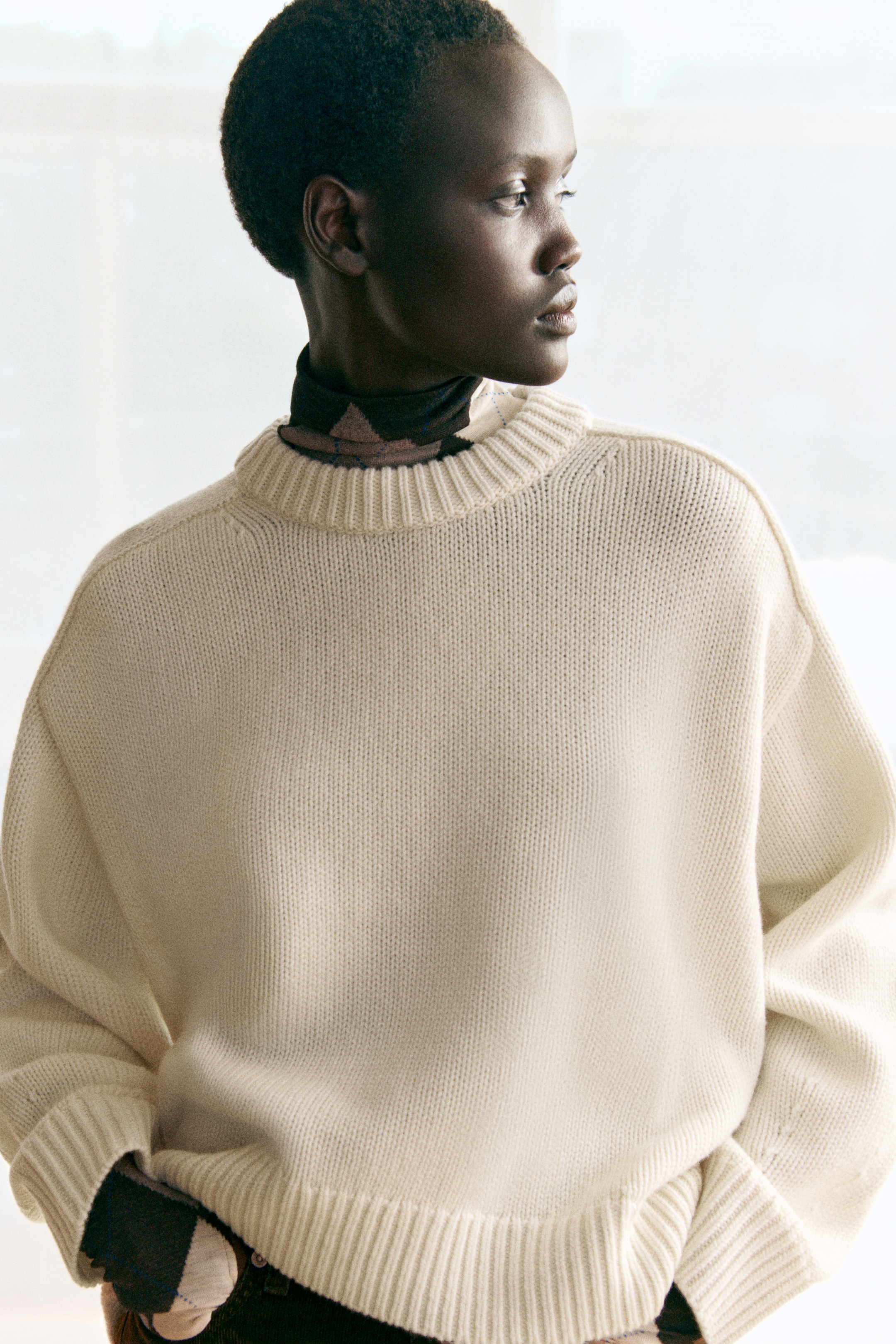 Person wearing a cream sweater, looking to the side, with a soft-focus background.