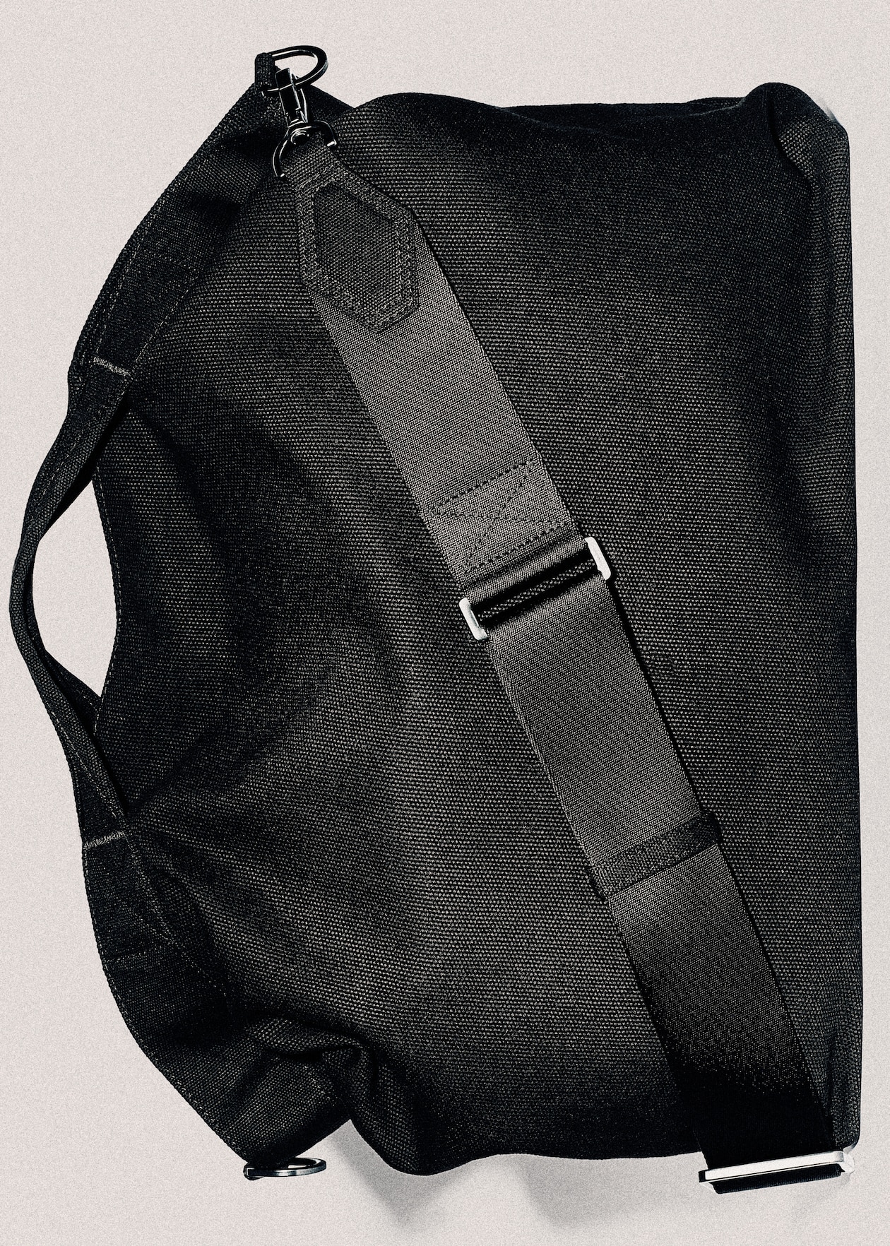 Black duffel bag with an adjustable shoulder strap and metal hook, displayed against a neutral background.