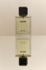 Placeholder for: Perfume bottle labeled "Solaire" with dark cap, reflected on a glossy surface, creating a mirrored effect.