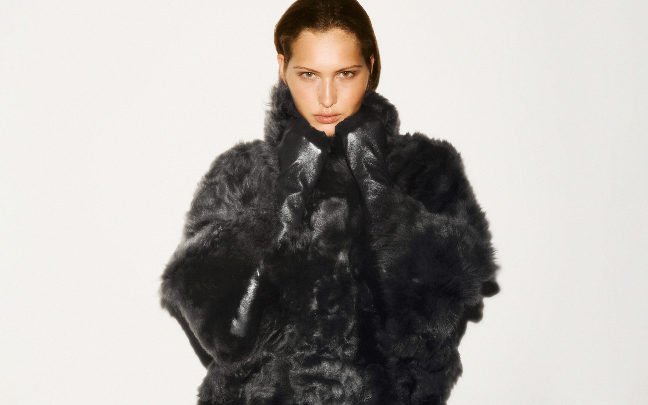 Person wearing a dark, plush fur coat, looking directly at the camera against a plain white background.