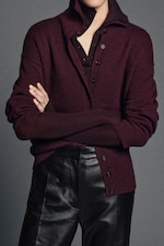 Placeholder for: Person wearing a dark burgundy layered top, with sleeves rolled up, over black leather pants, standing with arms crossed.