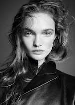 Placeholder for: Black and white portrait of a person with wavy hair wearing a leather jacket, looking directly into the camera with a neutral expression.