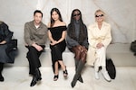 Placeholder for: Four people seated on a bench, dressed in stylish, modern attire, posing for a photo against a light-colored background.