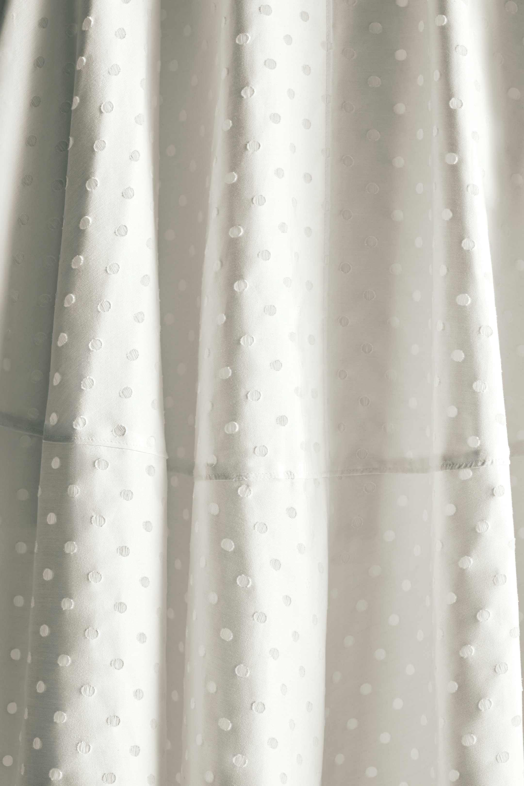Close-up of white fabric with a textured polka dot pattern, capturing light and shadow on the material's surface.