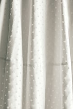 Placeholder for: Close-up of white fabric with a textured polka dot pattern, capturing light and shadow on the material's surface.