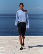 Placeholder for: Person walking outdoors by the sea, wearing a light blue off-shoulder top, dark shorts, black sandals, and a headband, with a serene ocean backdrop.