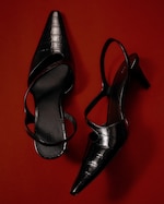 Placeholder for: Pair of black, pointed-toe high heels with a crocodile texture on a red background.