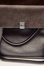 Placeholder for: Close-up of a luxury handbag with a dark leather body and a brown suede flap, featuring a silver lock.