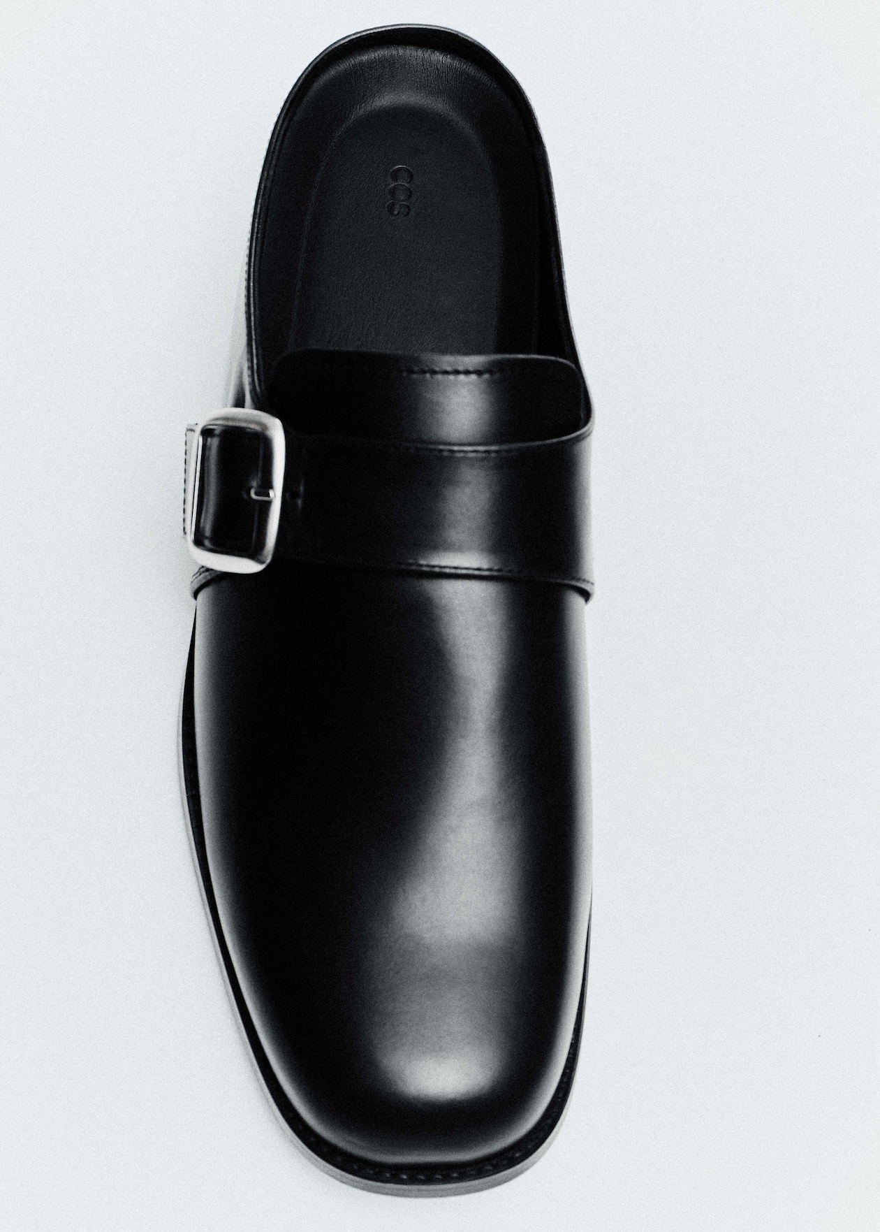 A black leather shoe with a shiny finish and a side buckle, viewed from above on a light background.