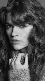 Placeholder for: Black and white close-up portrait of a person with wavy hair, wearing a cozy sweater, gazing directly at the camera.
