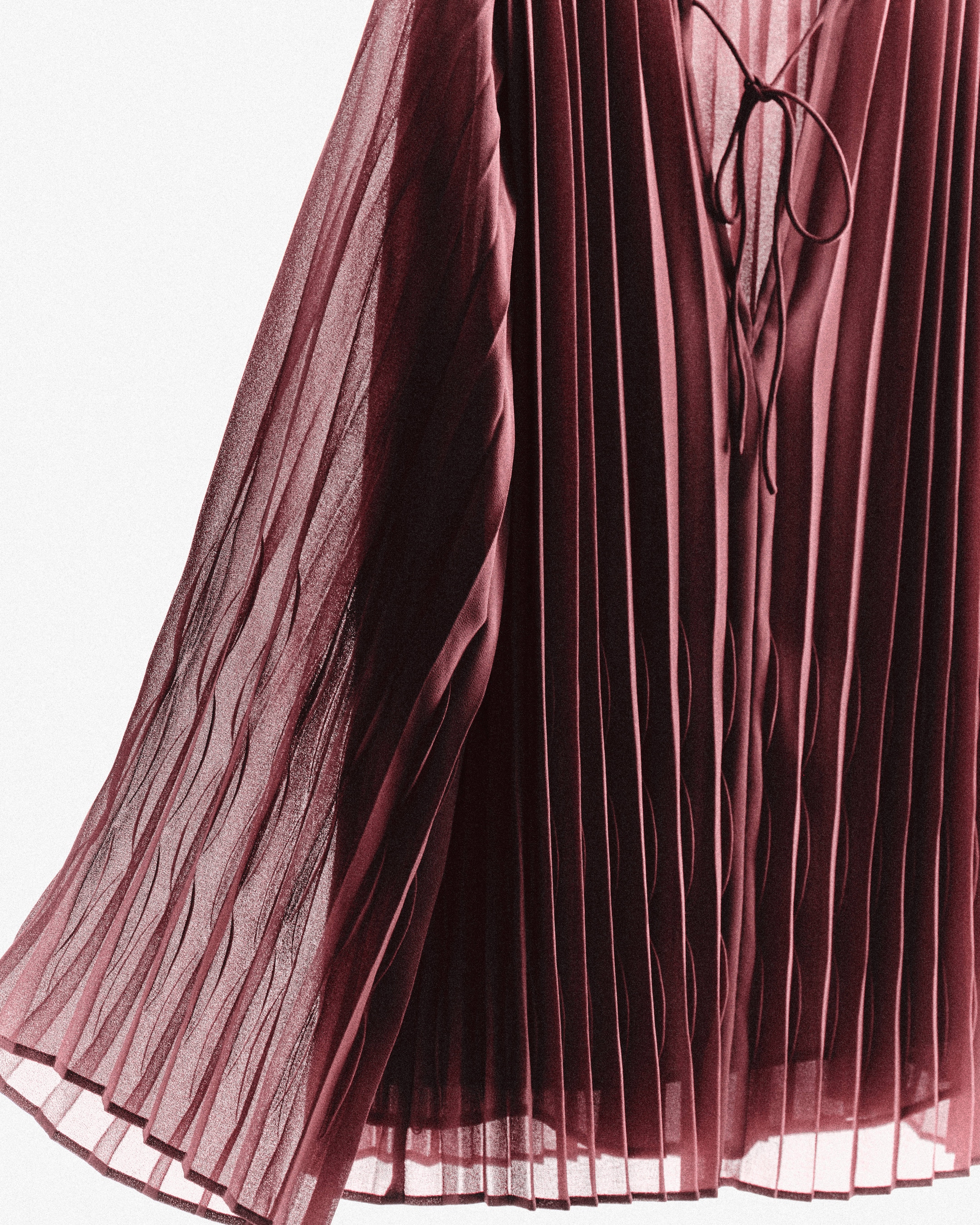 Close-up of a burgundy pleated dress with a tie detail at the neckline, displaying flowing fabric and elegant draping.