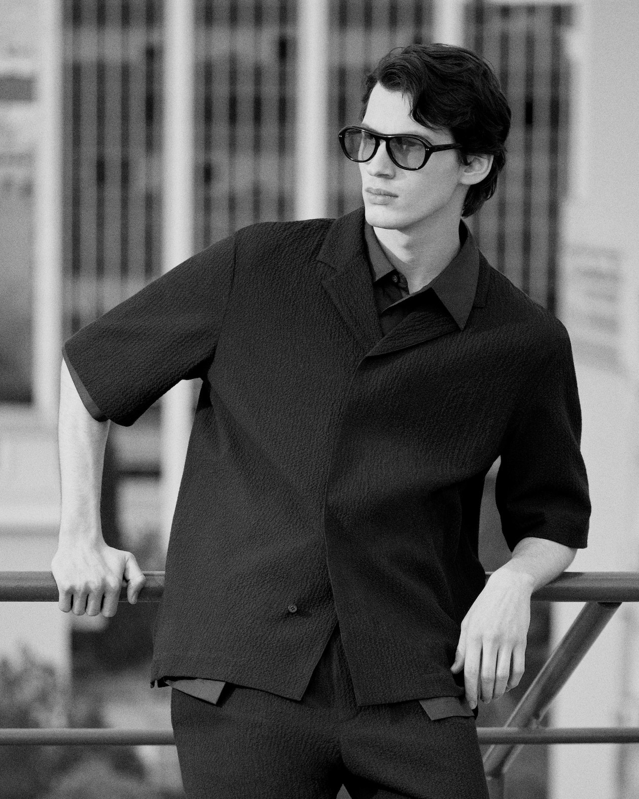 MAN LEANING ON FANCY IN BLACK SHORT SLEEVE SHIRT AND SUNGLASSES