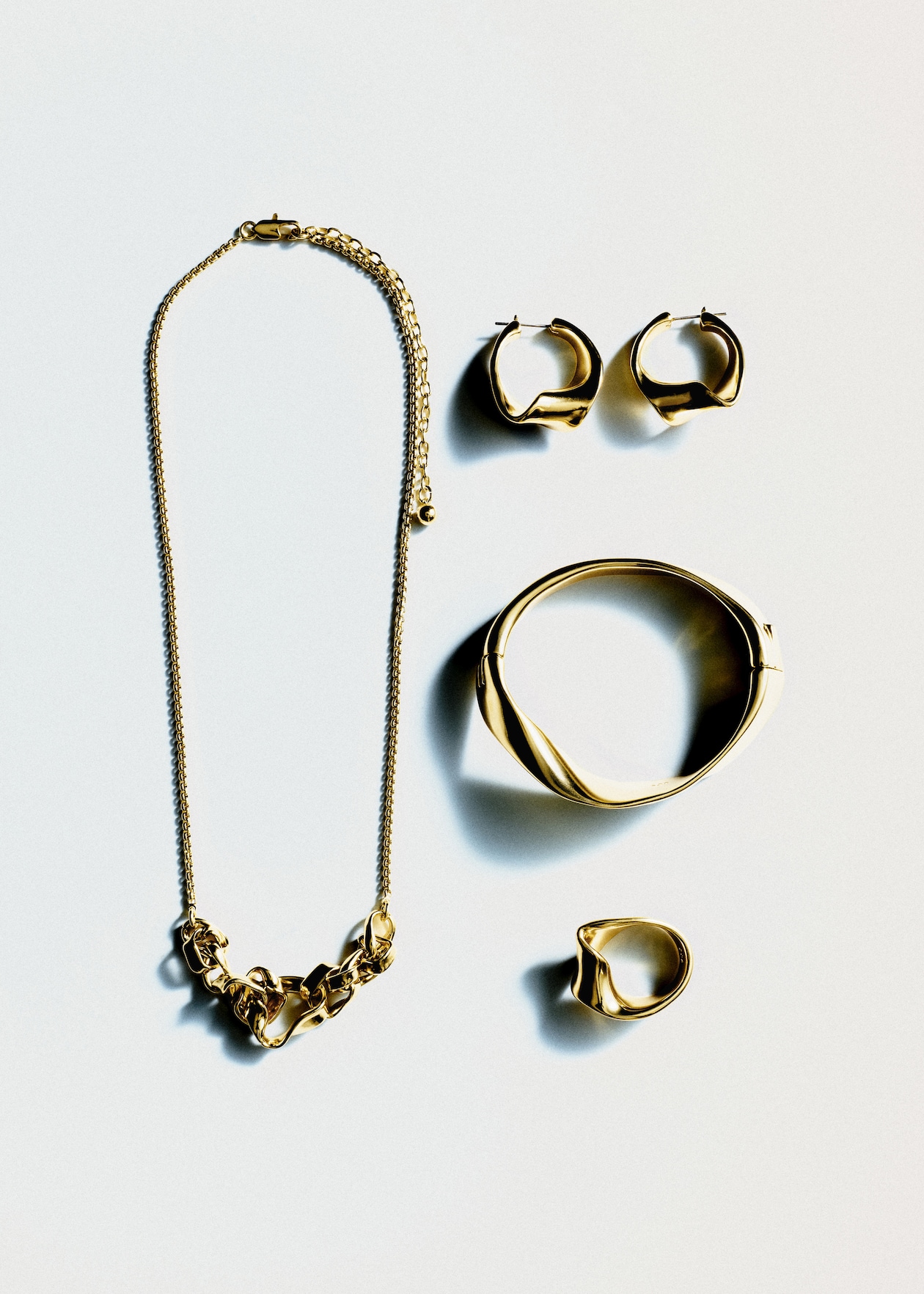 A set of gold jewelry including a necklace, bracelet, ring, and a pair of hoop earrings arranged on a white background.