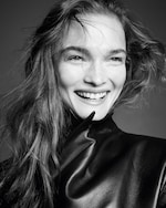Placeholder for: Woman smiling in a black and white portrait, wearing a leather jacket, with wavy hair and natural lighting.