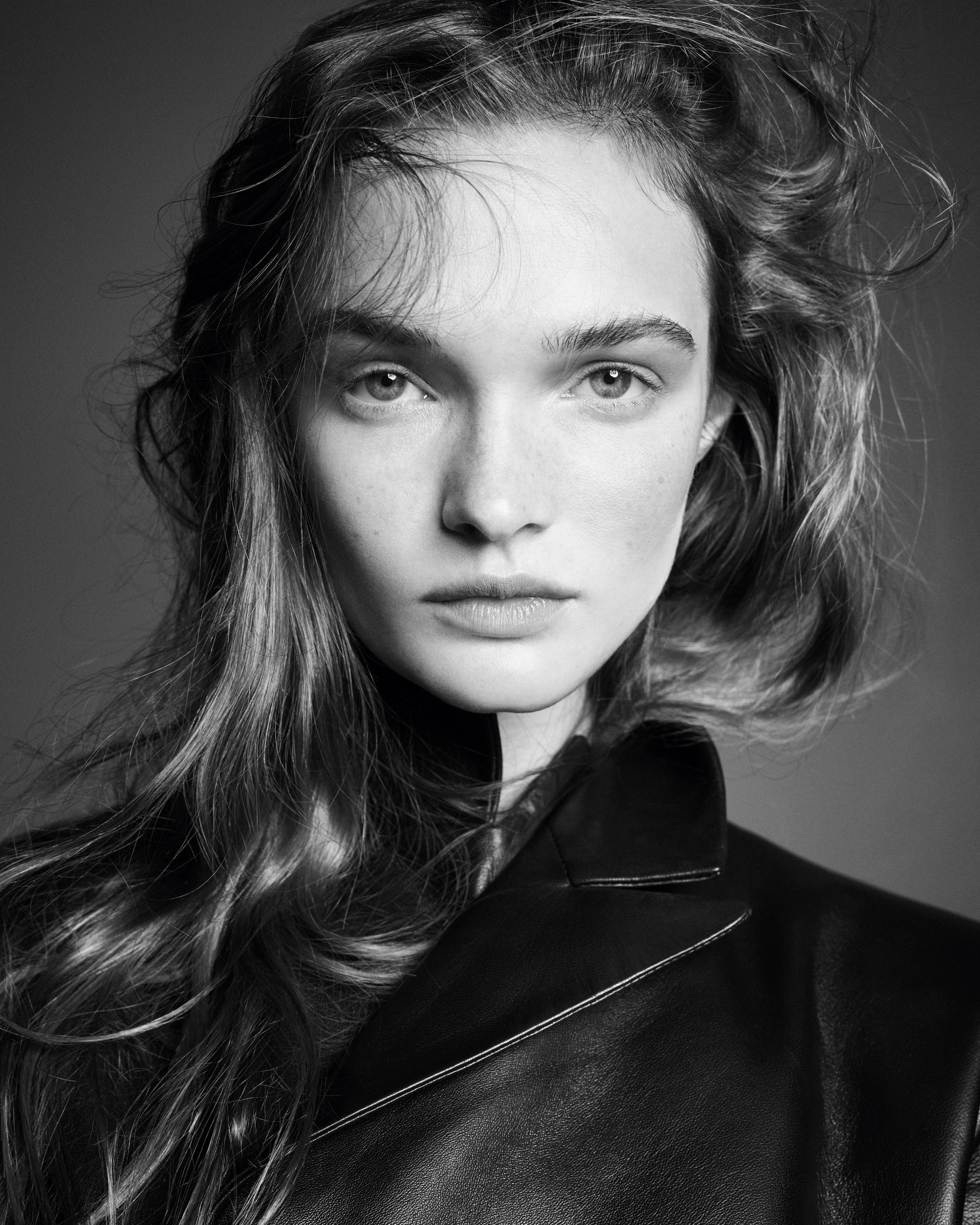 Black and white portrait of a person with long hair and a serious expression, wearing a leather jacket against a plain background.