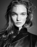 Placeholder for: Black and white portrait of a person with long hair wearing a leather jacket, looking directly at the camera with a neutral expression.