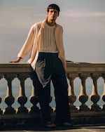 Placeholder for: Man in striped knitted top and overshirt leaning on a stone balcony