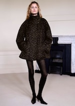 Placeholder for: A model wearing a leopard-print coat and black striped tights stands in a room with a fireplace.